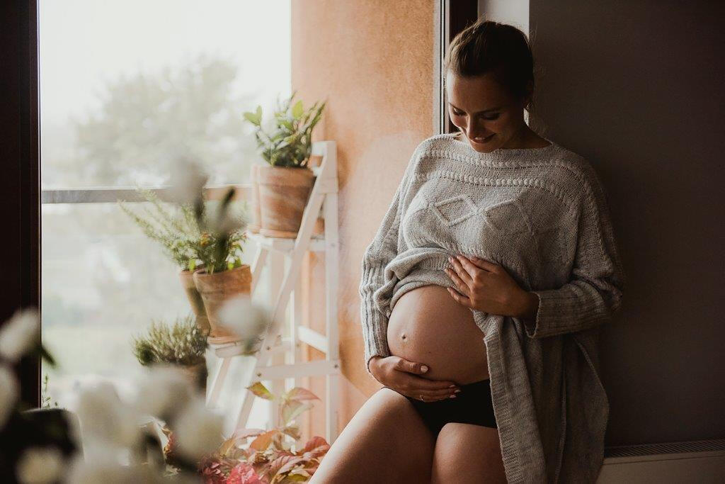 Naturalna sesja ciążowa w Krakowie – zbliżenie na dłonie przyszłej mamy trzymającej nagi brzuszek, profesjonalna fotografia brzuszkowa Anna Janowska.